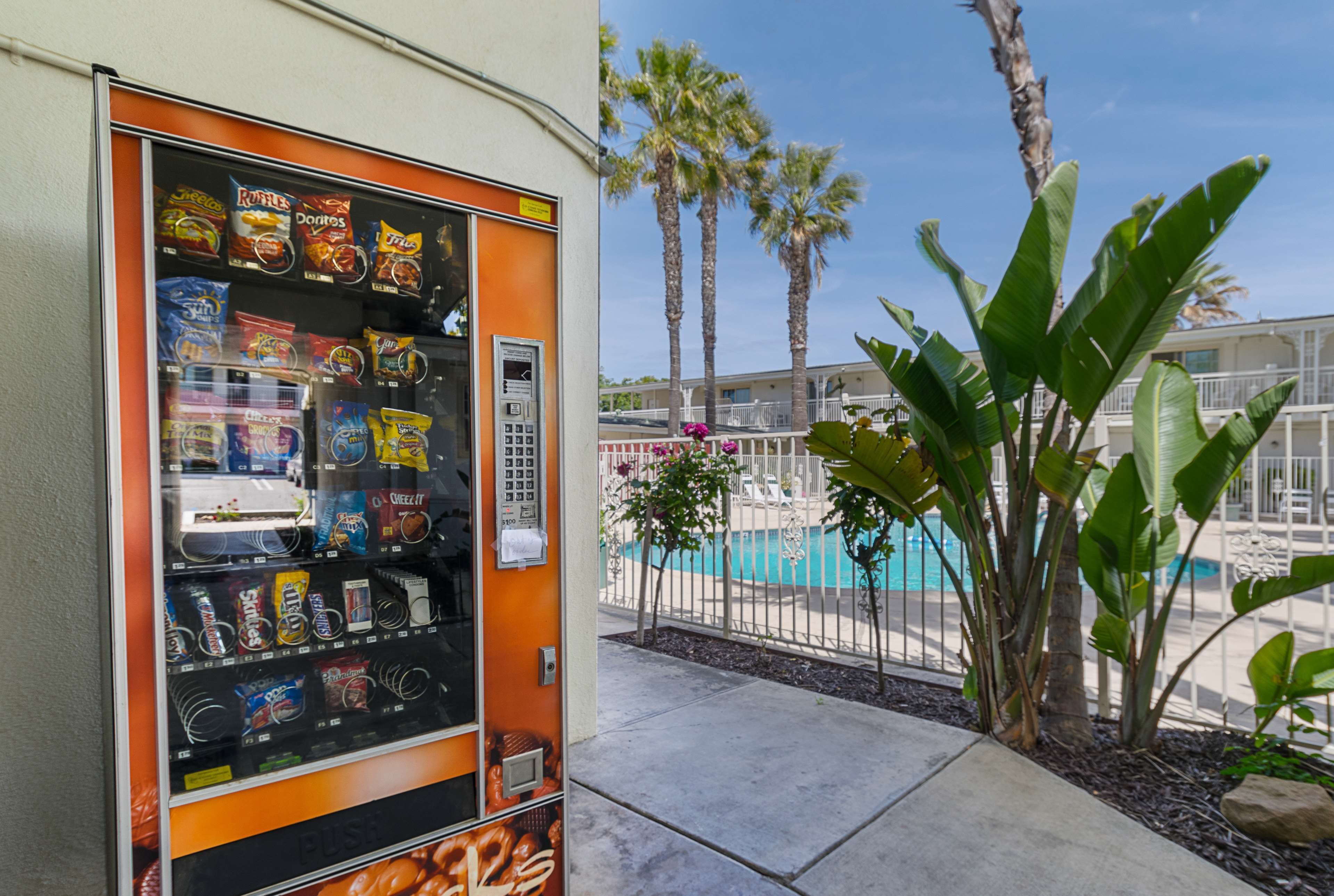 Ein Getränkeautomat mit Snacks und ein Poolbereich mit Palmen und einem Zaun.