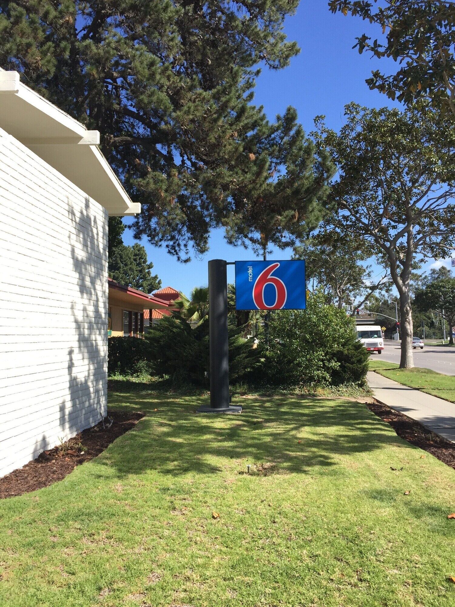 A motel sign with the number 6, surrounded by greenery and a white building.