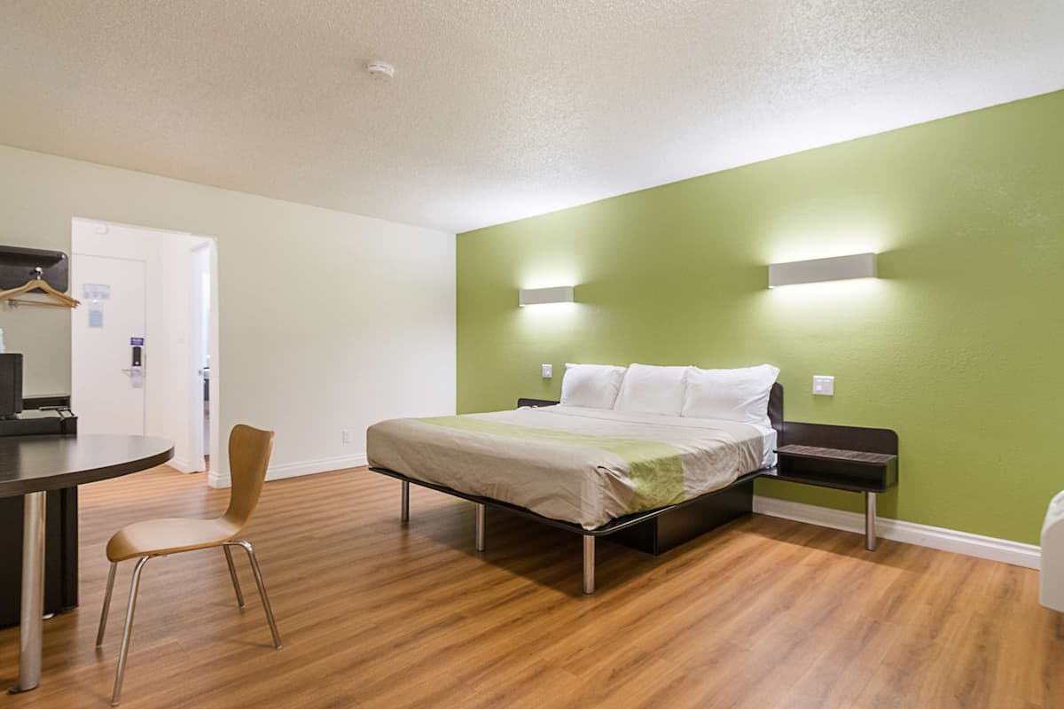 A hotel room with a bed, a chair, a desk, and a green wall.
