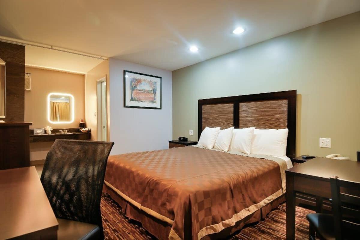 A hotel room with a large bed, a desk, a chair, and a bathroom with a mirror.