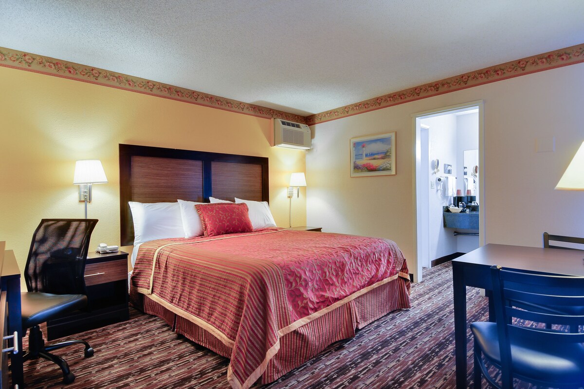 A hotel room with a bed, desk, chair, and a small table.