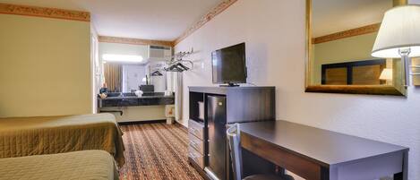A hotel room with two beds, a desk, a television, a mirror, and a lamp.