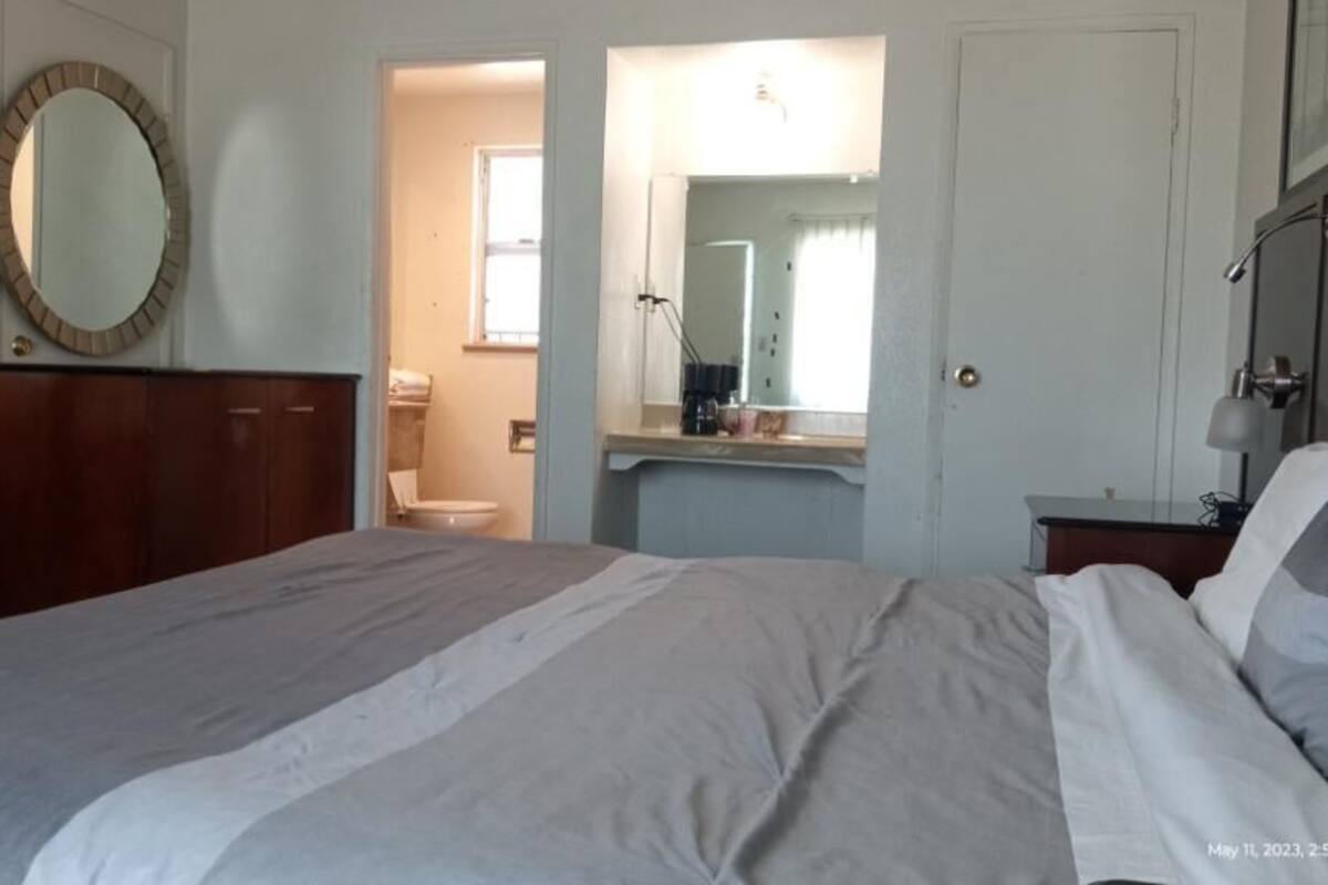 A bedroom with a bed, a dresser, a mirror, and a bathroom visible through an open door.