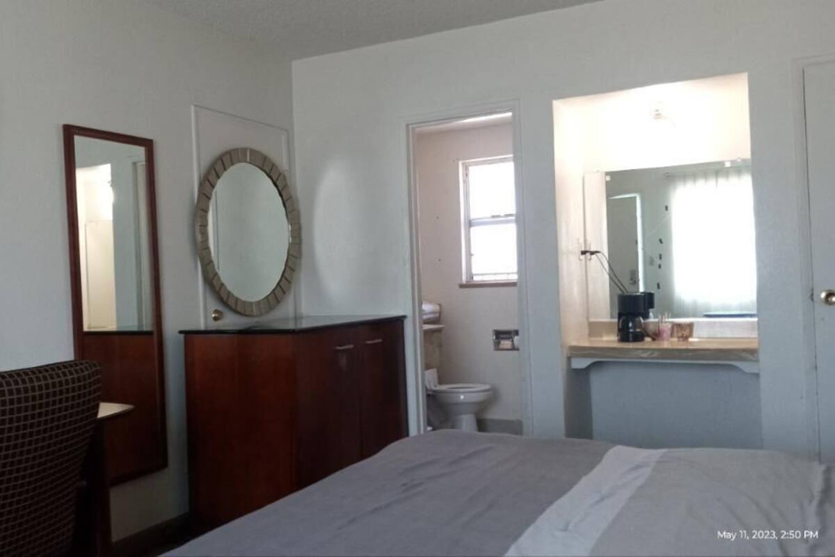 A hotel room with a bed, a desk, a chair, a wardrobe, a mirror, a toilet, and a window.
