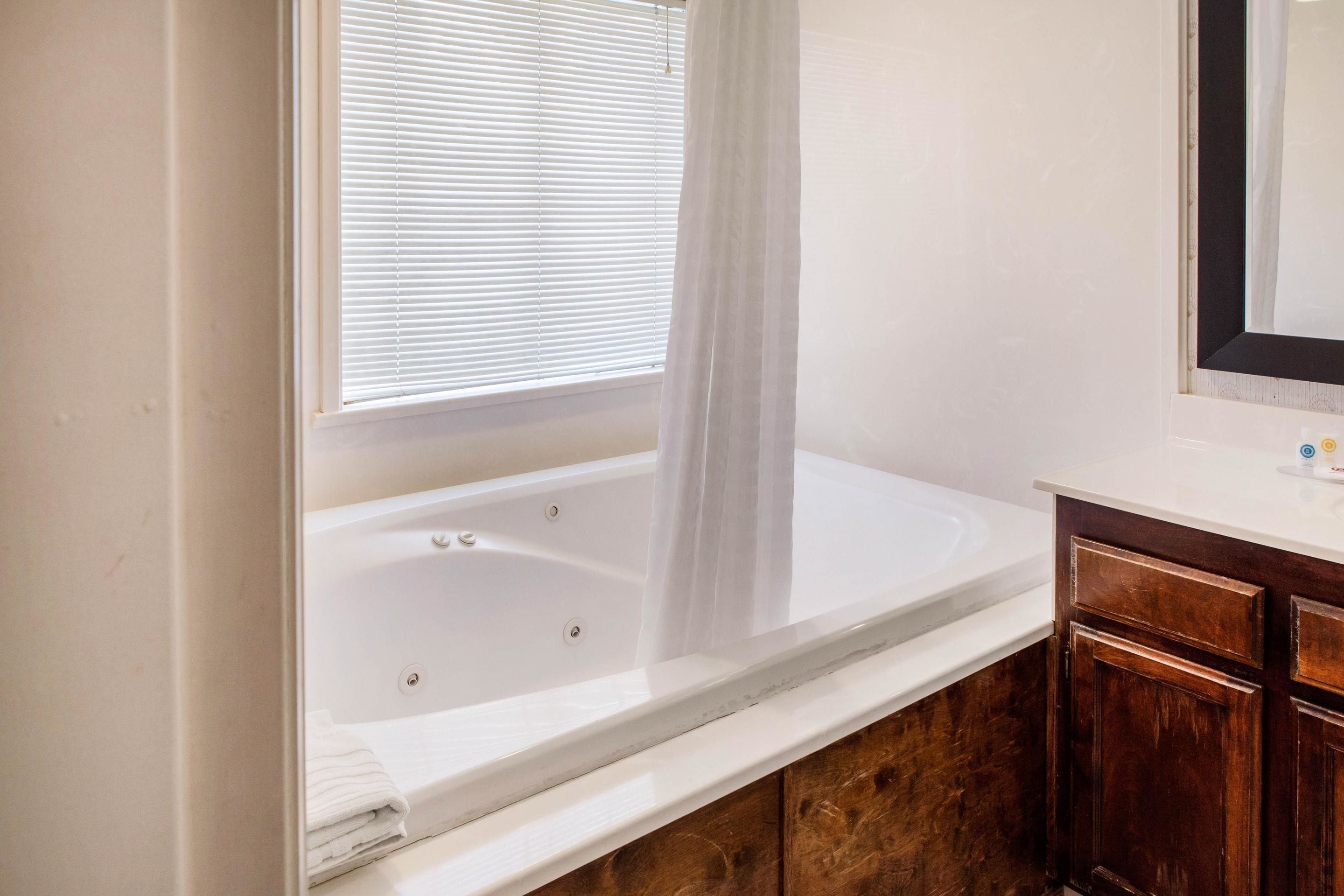 A bathroom with a white bathtub, wooden cabinets, and a window with blinds.