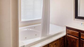 A bathroom with a white bathtub, wooden cabinets, and a window with blinds.