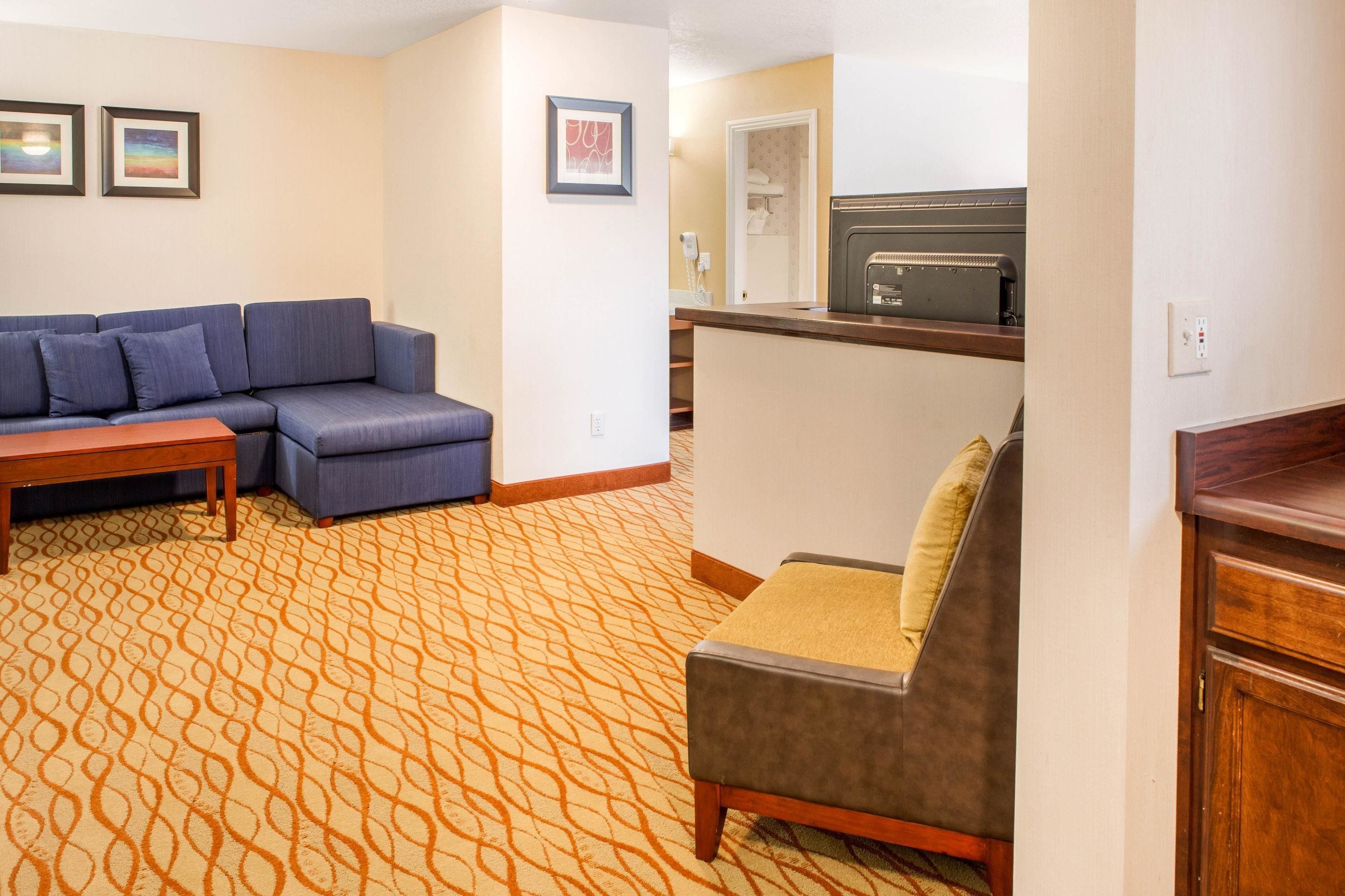 A hotel room with a sofa, a small table, a kitchenette, and a patterned carpet.
