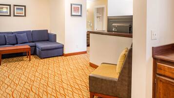 A hotel room with a sofa, a small table, a kitchenette, and a patterned carpet.