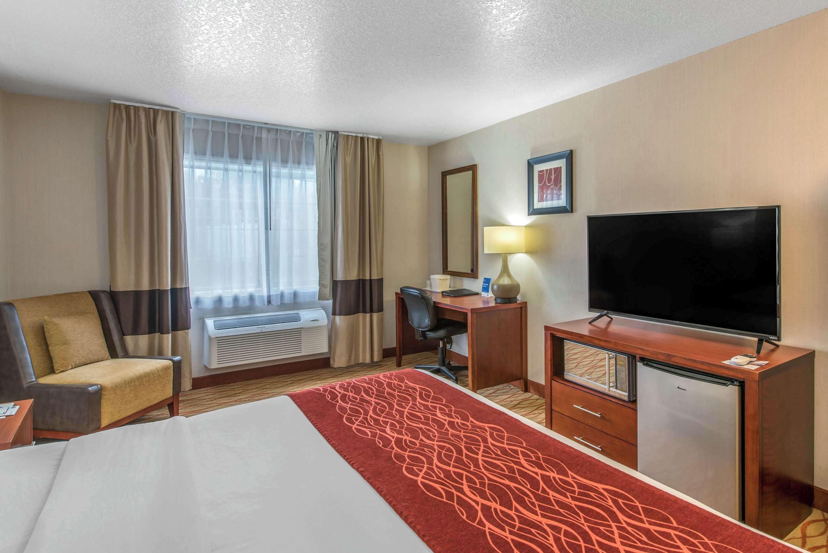 A hotel room with a bed, a desk, a television, a chair, and a window with curtains.