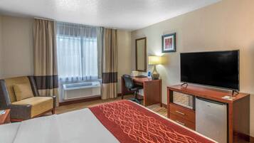 A hotel room with a bed, a desk, a television, a chair, and a window with curtains.
