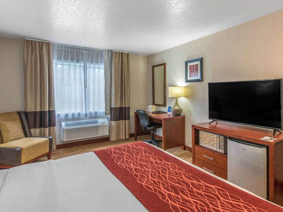 A hotel room with a bed, a desk, a television, a chair, and a window with curtains.