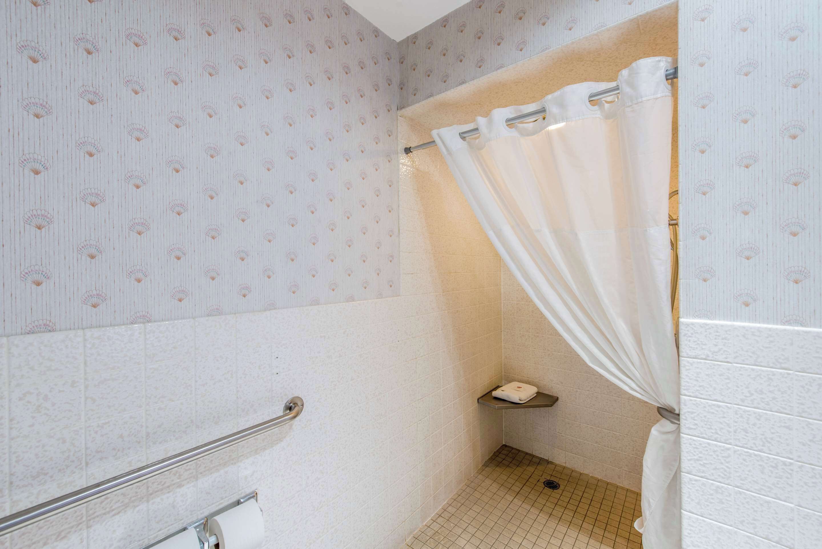 Une petite salle de bain carrelée, équipée d’un rideau de douche, d’un porte-serviettes et d’un support à papier toilette.