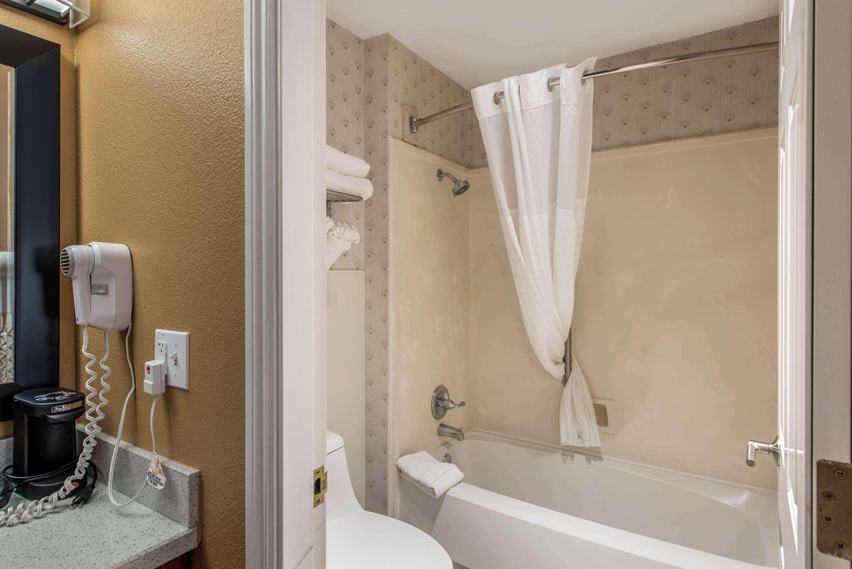 A bathroom with a bathtub, a toilet, a hairdryer, and a coffee maker.