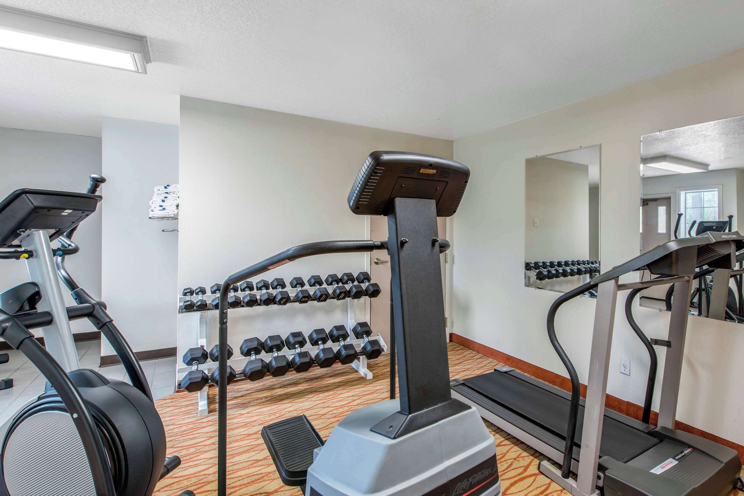 A gym with treadmills, dumbbells, and a mirrored wall.
