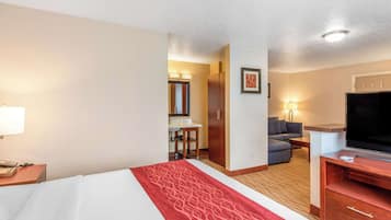 A hotel room with a bed, a desk, a television, a sofa, and a bathroom visible through an open door.