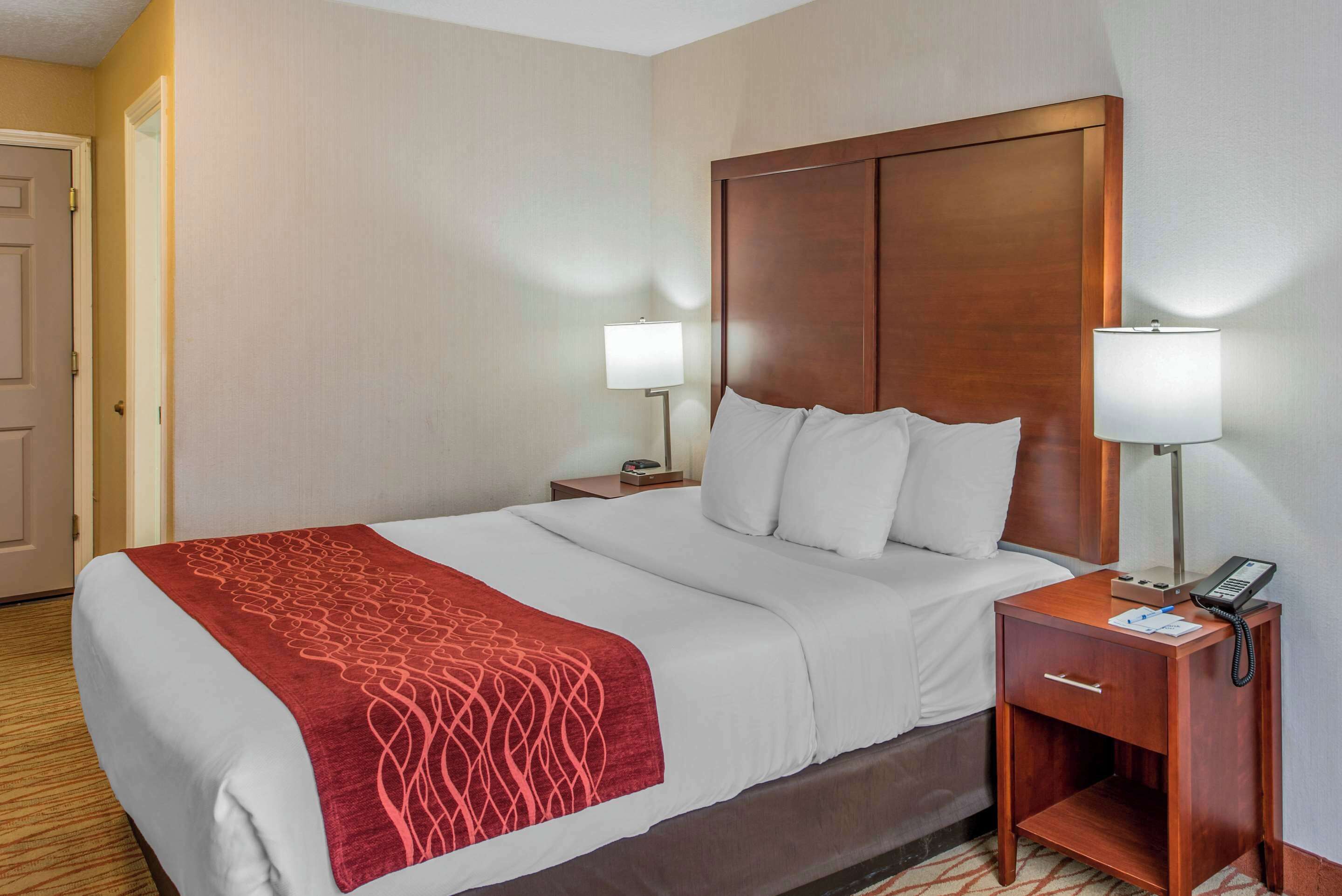 A hotel room with a large bed, two bedside tables, a wooden headboard, and two bedside lamps.