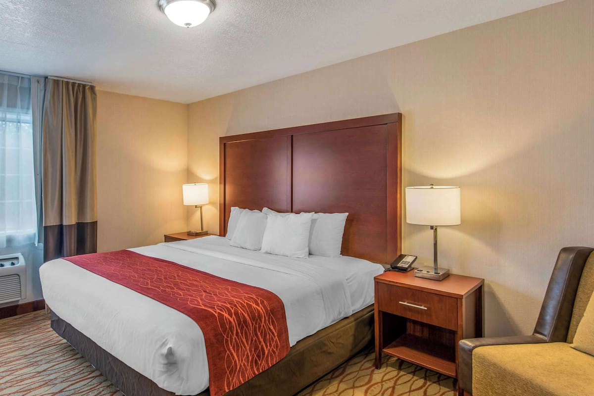 Une chambre d’hôtel avec un grand lit, deux tables de chevet avec des lampes, une chaise et une fenêtre avec des rideaux.