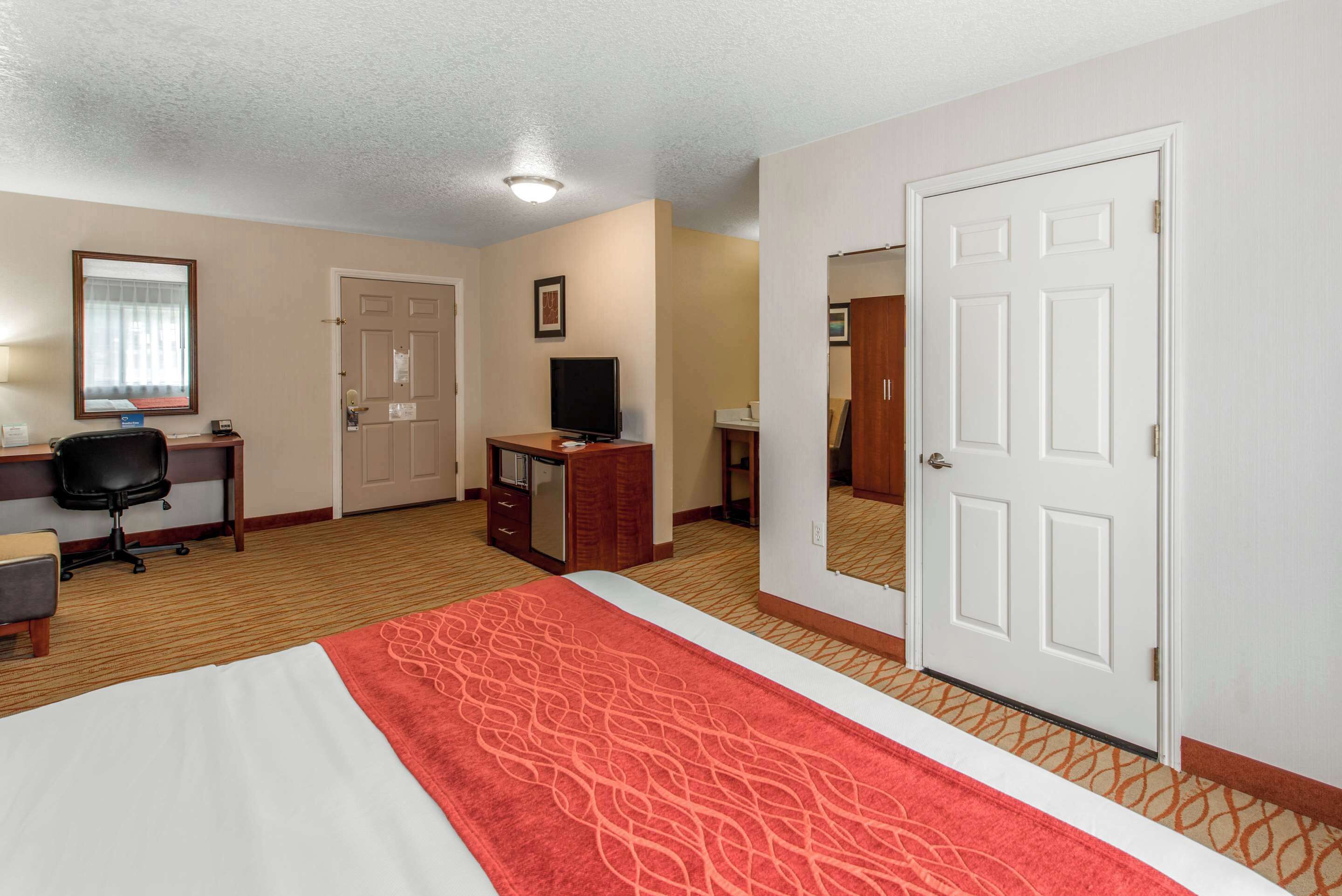 A hotel room with a bed, desk, chair, television, and a door.