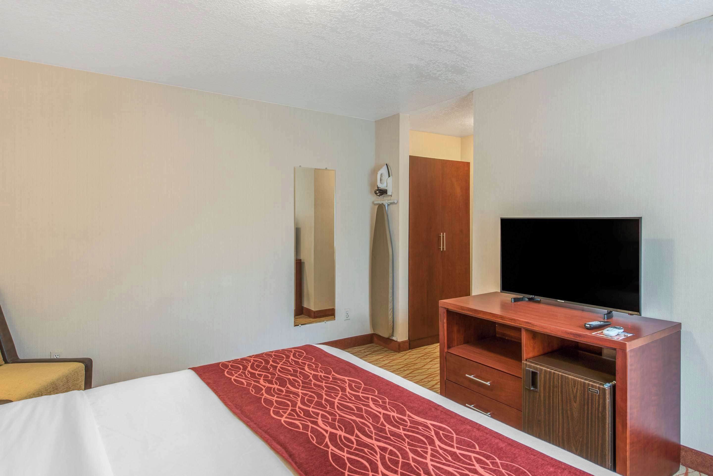 A hotel room with a bed, a TV, a wooden desk, and a wardrobe.
