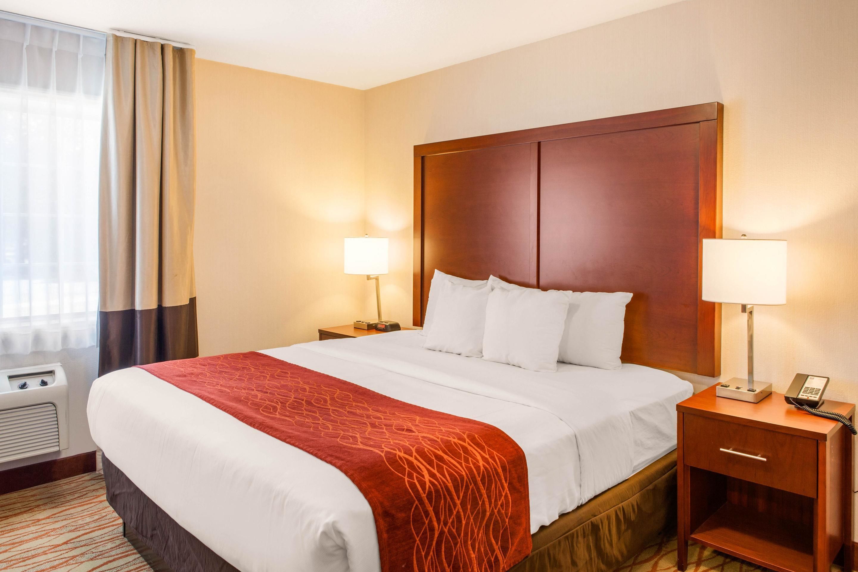 Habitación de hotel con una cama grande, dos mesitas de noche con lámparas, un calentador y una ventana con cortinas.