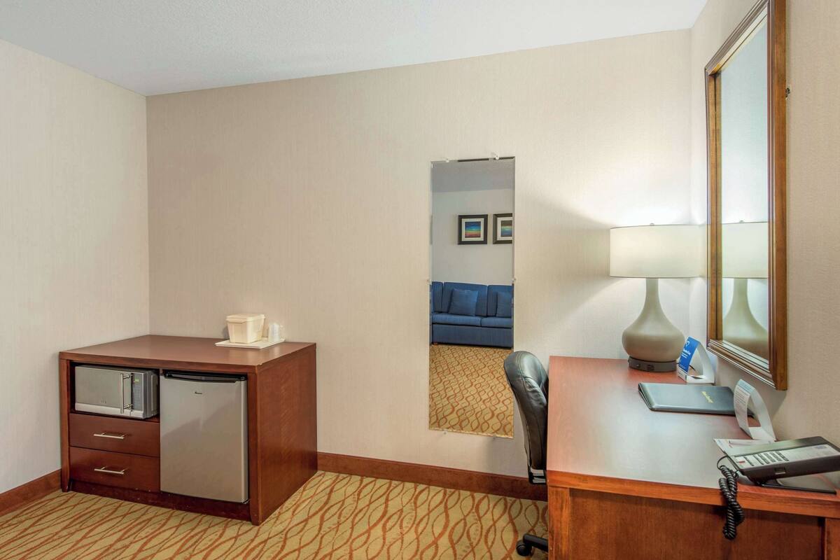 Une chambre d’hôtel avec un bureau en bois, un petit réfrigérateur, un miroir, une lampe et un téléphone.
