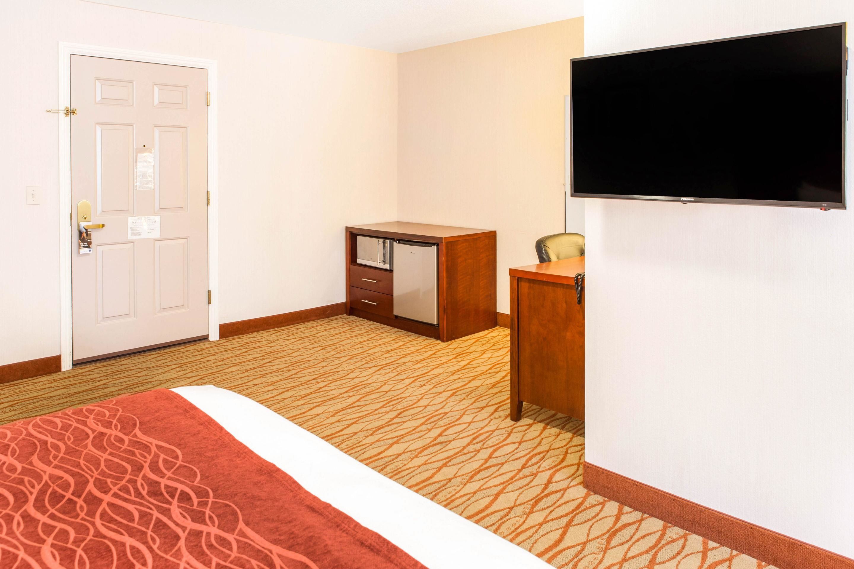 A hotel room with a bed, a desk, a television, and a door.
