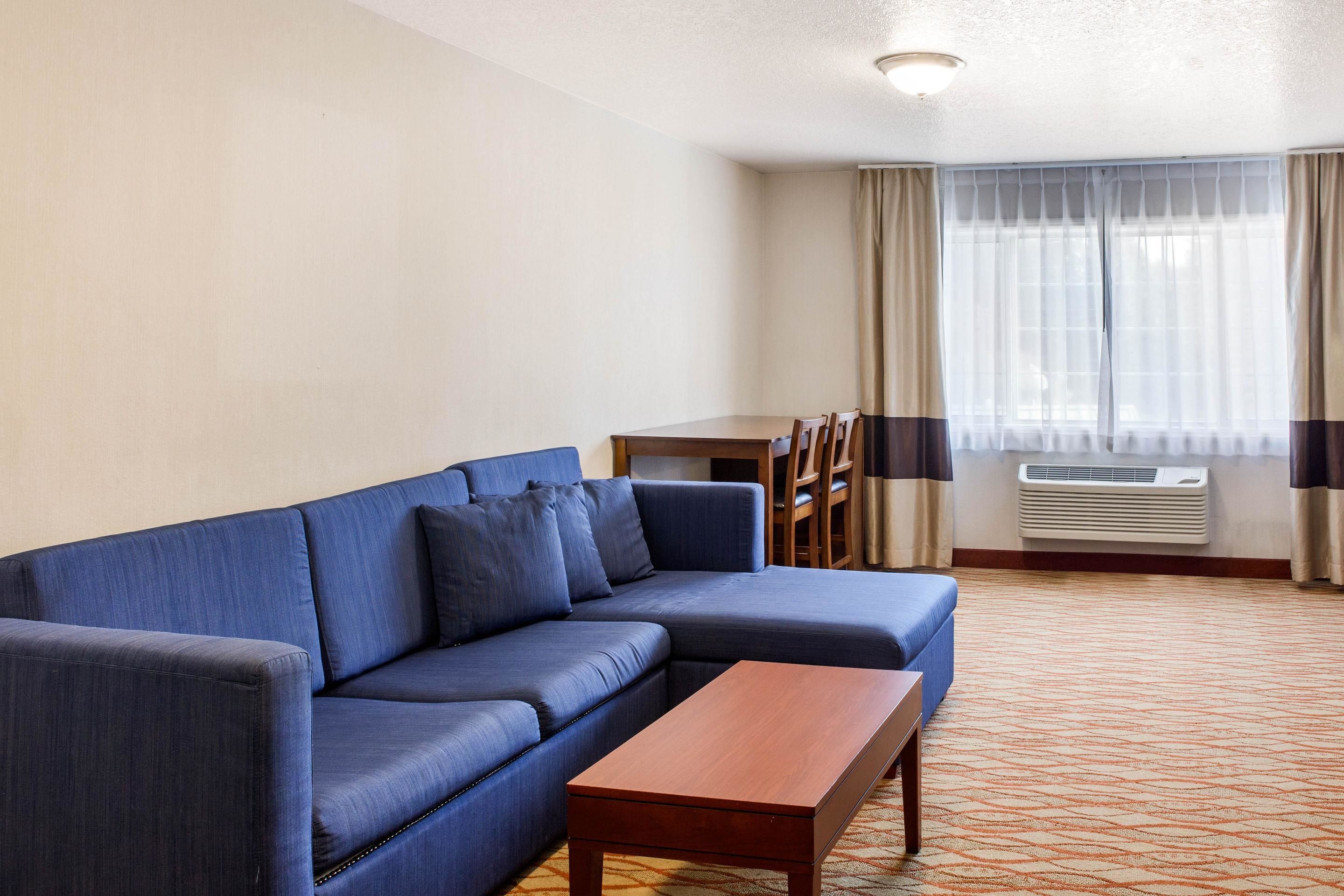 A living room with a blue sofa, a wooden coffee table, a dining table with chairs, and a window with curtains.