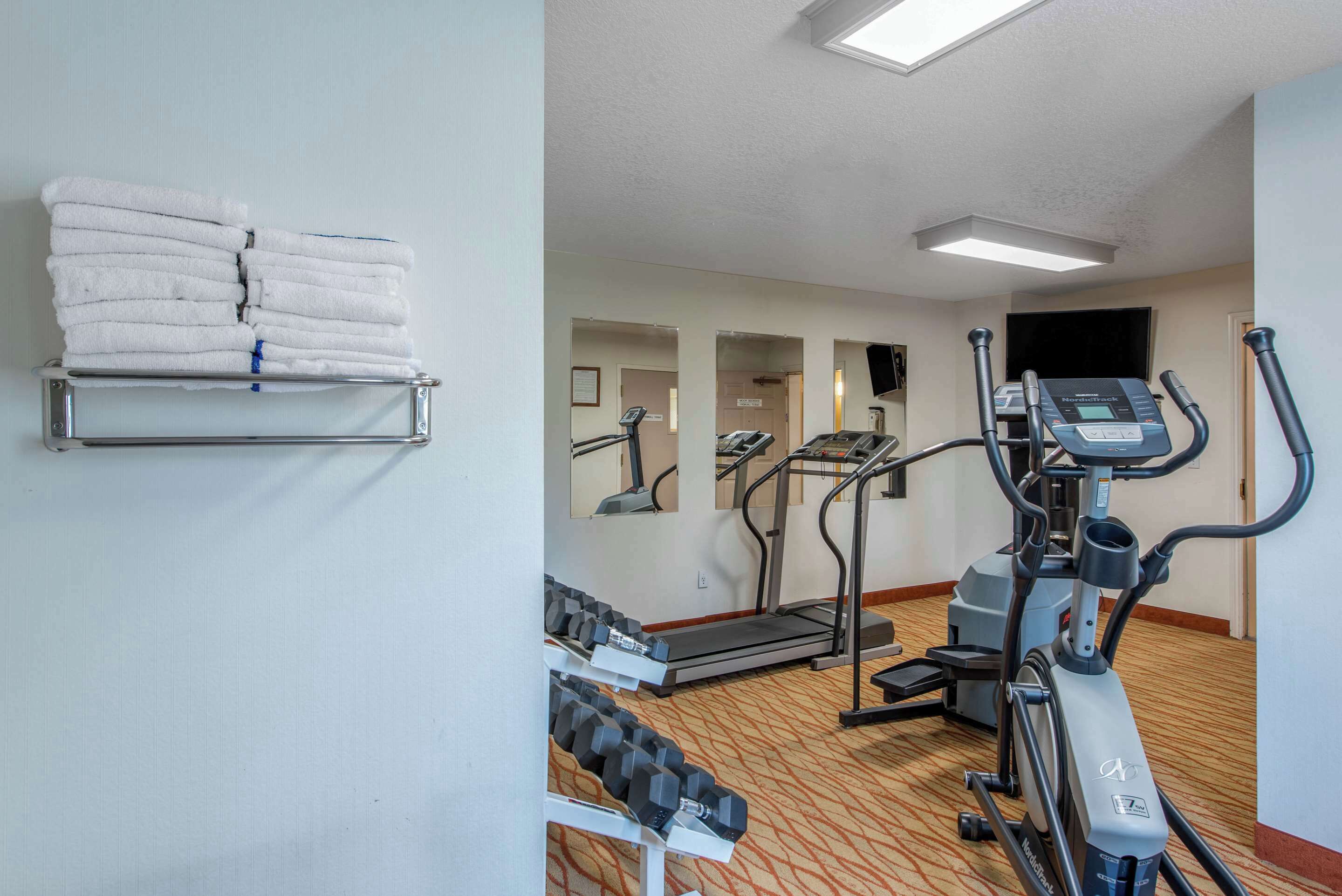 A hotel gym with exercise equipment, towels on a rack, and a carpeted floor.