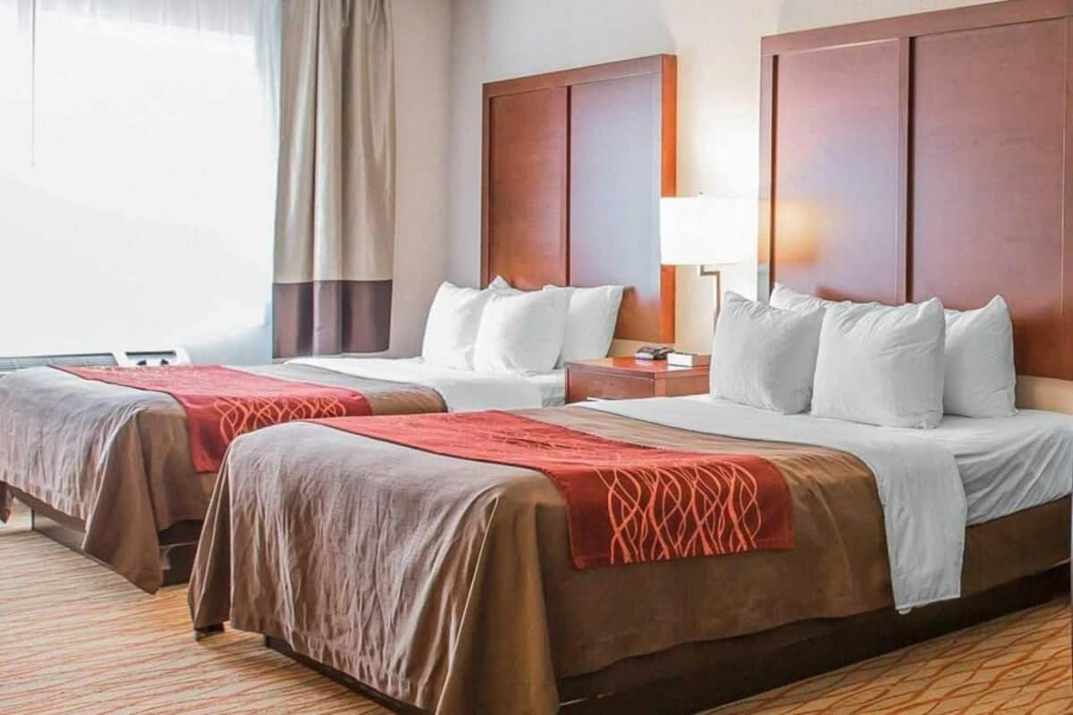 Une chambre d’hôtel avec deux lits, une table de chevet, une lampe et une fenêtre avec des rideaux.