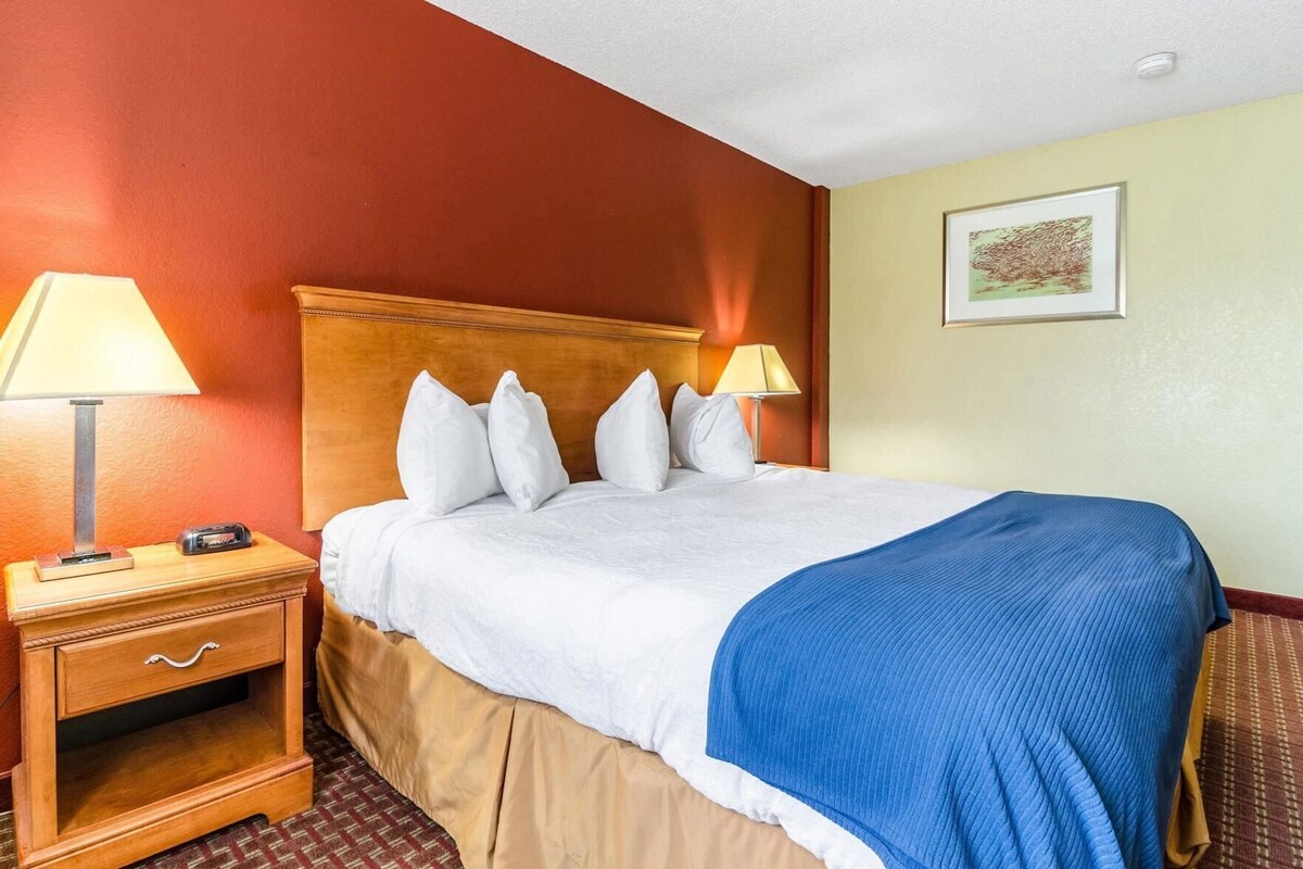 A hotel room with a bed, two bedside tables, a lamp on each table, a blue blanket, and a framed picture on the wall.