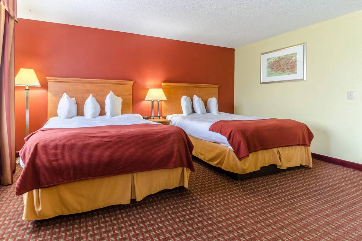 A hotel room with two beds, each with a red and yellow bedspread, a wooden headboard, and a lamp beside each bed.