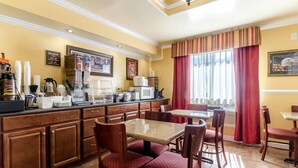 Un espace pour le petit-déjeuner dans un hôtel, avec des meubles en bois, un comptoir équipé pour préparer le café et des chaises à l’assise rembourrée de couleur rouge.