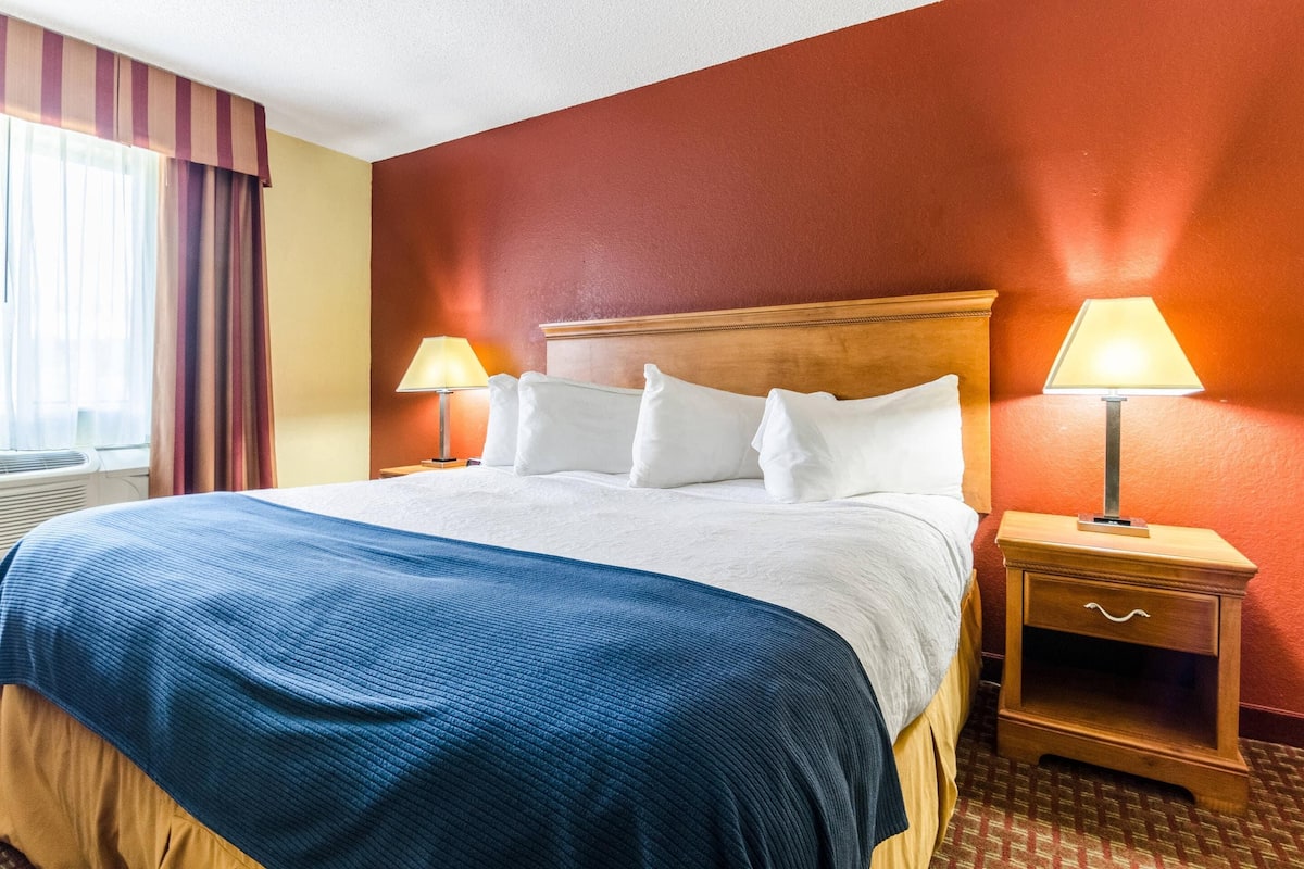 A hotel room with a large bed, two bedside lamps, a wooden nightstand, and a window with curtains.