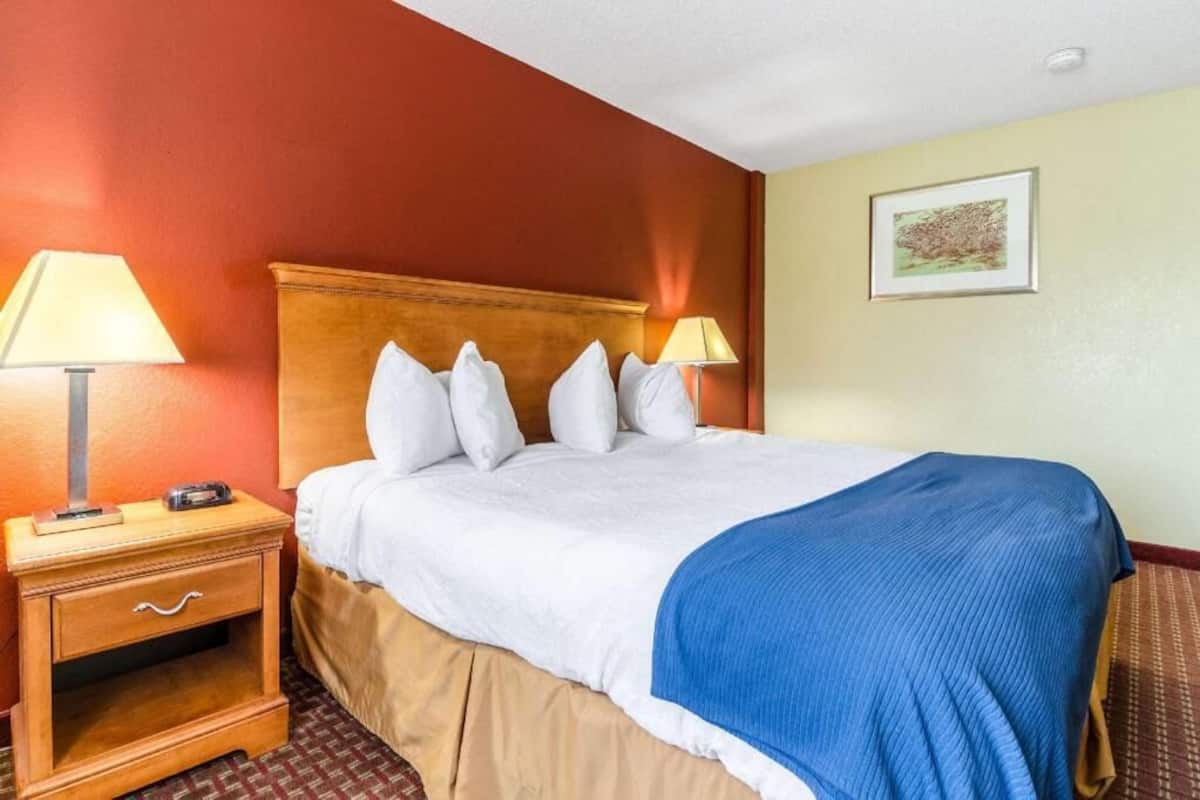A hotel room with a bed, two bedside lamps, a nightstand, and a framed picture on the wall.