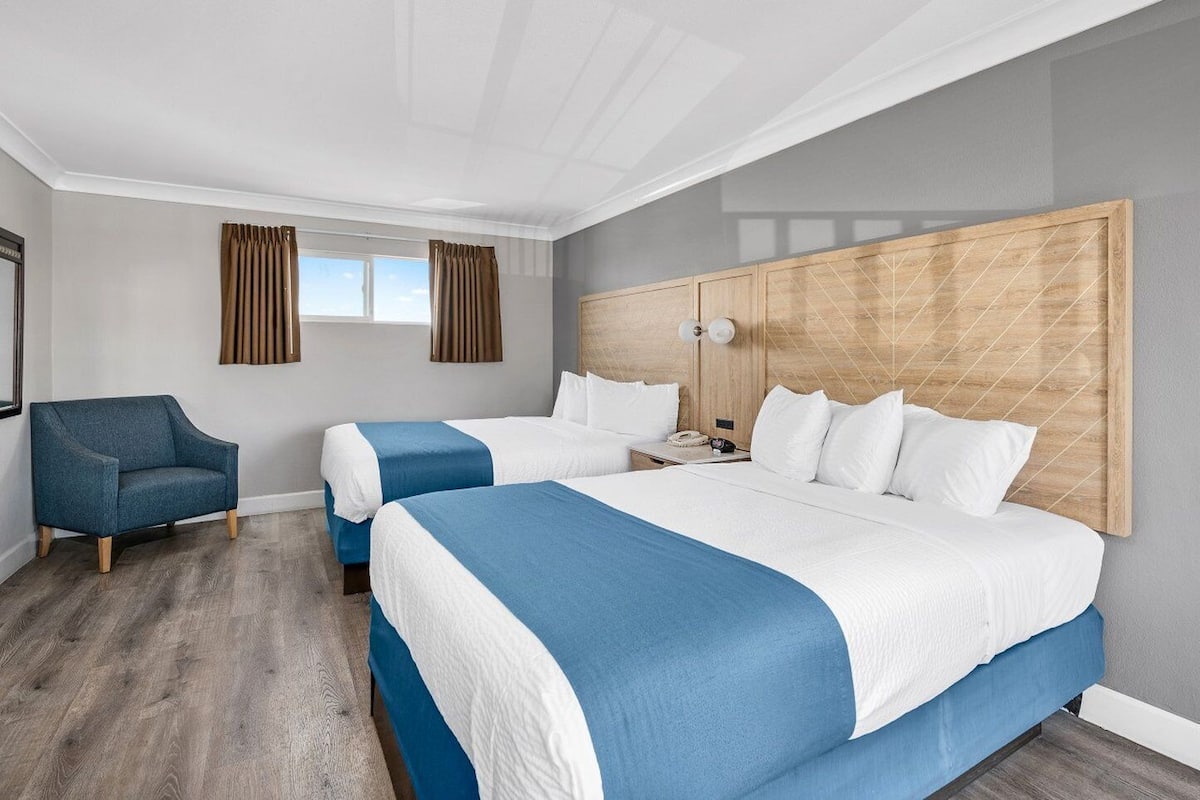 A hotel room with two beds, a blue armchair, and a wooden headboard.