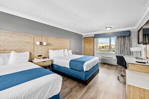 Ein Hotelzimmer mit zwei Betten, einem Schreibtisch, einem Stuhl, einem Fernseher und einem Fenster mit Vorhängen.