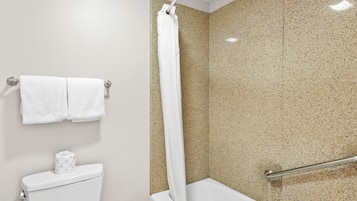 Un baño con inodoro blanco, ducha con pared beige salpicada y toalla blanca colgada en un toallero metálico.