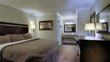 A hotel room with a large bed, a bedside table, a mirror, and a bathroom vanity.