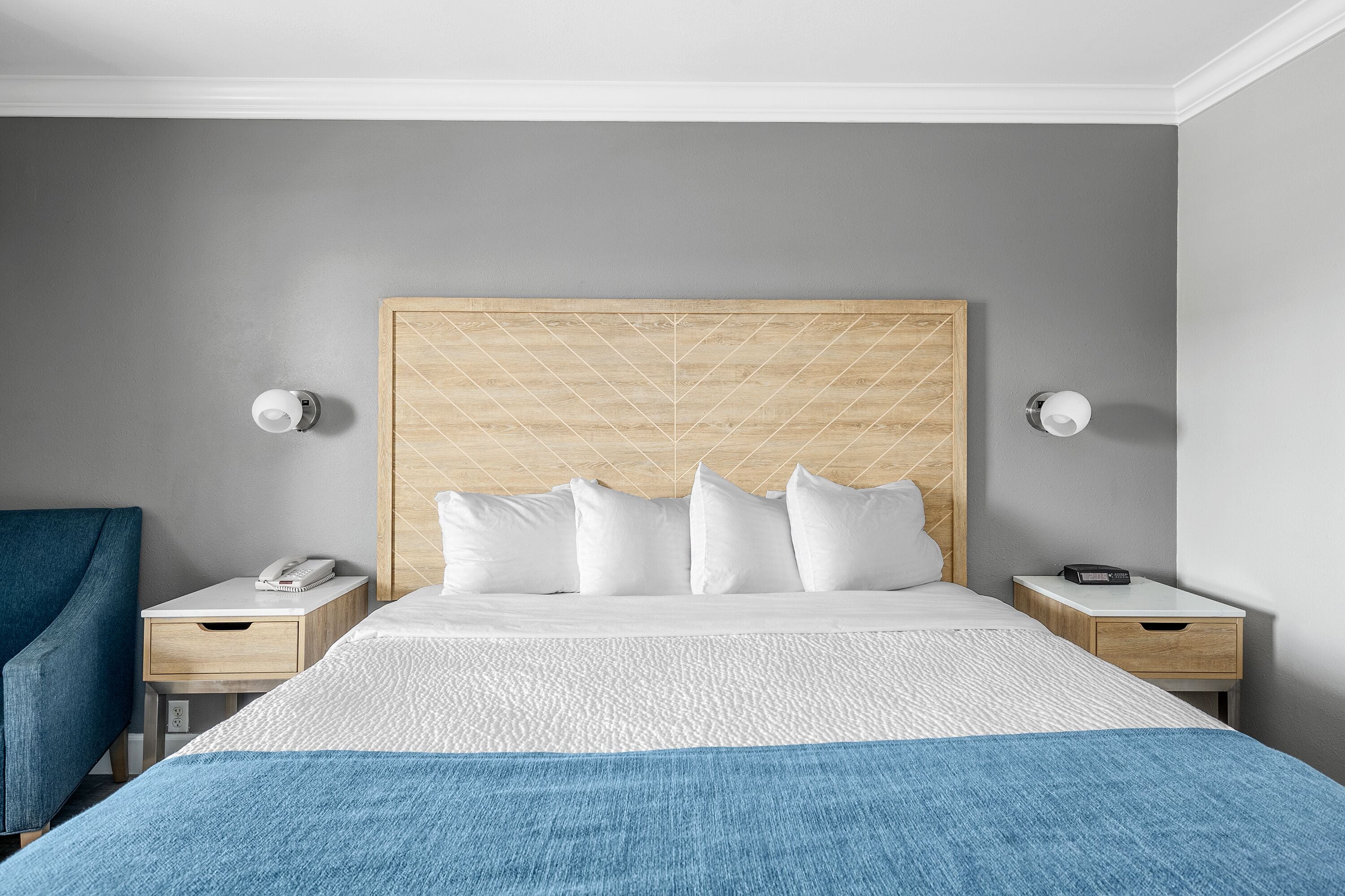 Una habitación de hotel con una cama grande, dos mesitas de noche, un cabecero de madera y una manta azul.
