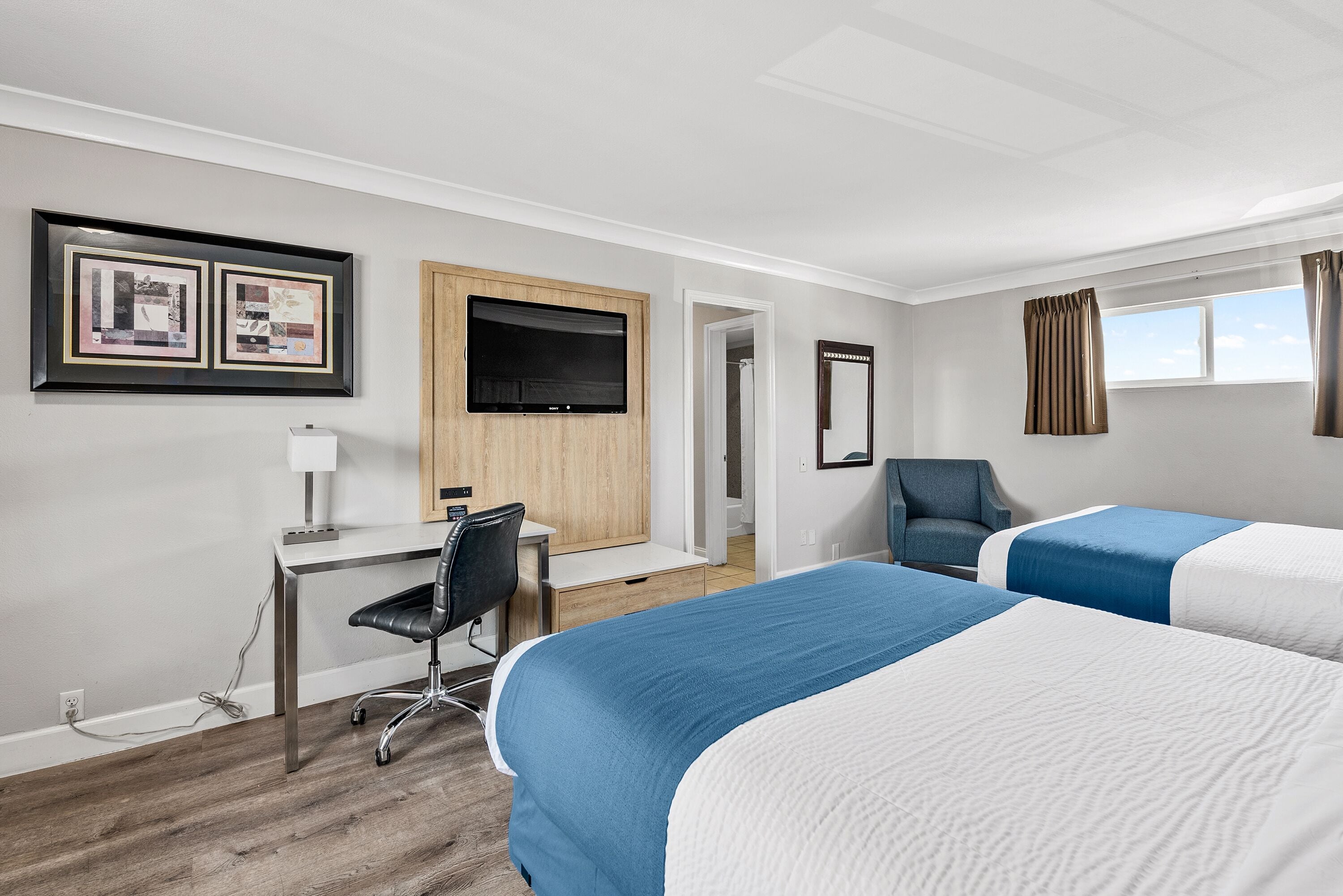 Una habitació d'hotel amb dos llits, un escriptori amb una cadira, un televisor i quadres a la paret.