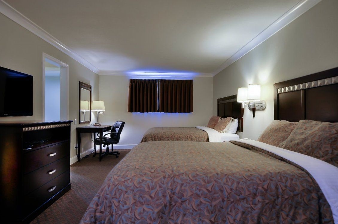 Habitación de hotel con cama, escritorio, silla, televisor y ventana con cortinas.