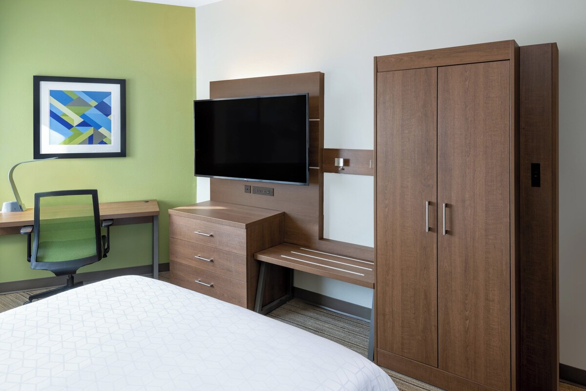 A hotel room with a bed, a desk, a chair, a TV, and a wardrobe.