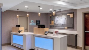Uma área de recepção com dois balcões, um painel digital e um espelho grande.