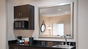 A modern kitchen with dark wooden cabinets, a built-in microwave, a coffee maker, and a sink with a mirror above it. - Hampton Inn Loveland (Loveland)