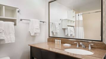 A bathroom with a large mirror, a granite countertop sink, and white towels.