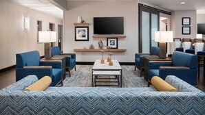 A hotel lobby with a large sofa, multiple armchairs, a coffee table, and a flat-screen TV mounted on the wall. - Hampton Inn Loveland (Loveland)