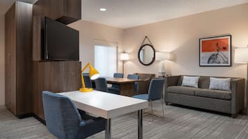 Una habitación de hotel moderna con una televisión de pantalla plana, una mesa de comedor con sillas, un sofá y un espejo grande.