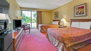 A hotel room with two beds, a TV, a desk, and a window with curtains.