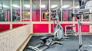 A gym with exercise equipment, a mirror, and a wall with a red and white color scheme.