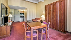 A hotel room with a dining table, chairs, a TV, a kitchen area, and a wardrobe.